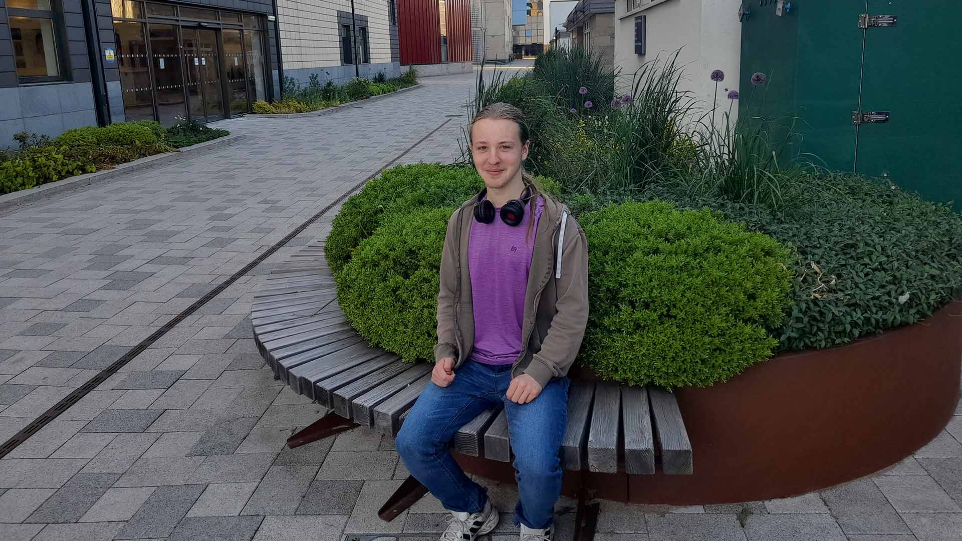 Nathan sat on a wooden bench with a large planter behind it.
